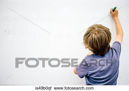 Stock Image - Young boy writing on whiteboard, rear view. Fotosearch