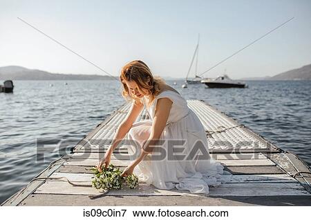 Stock Photo - Young bride in wedding dress laying bouquet on lake pier, Stresa, Piemonte, Italy. Fotosearch