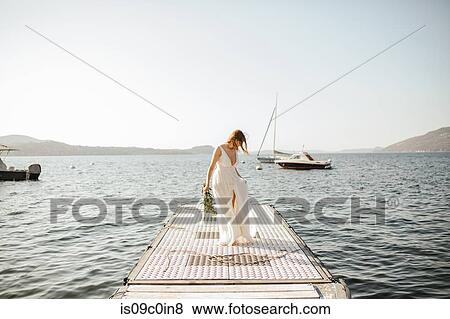 Stock Photo - Young bride in wedding dress strolling on windy lake pier, Stresa, Piemonte, Italy. Fotosearch
