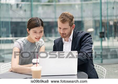 Stock Photo - Young businessman and woman looking at laptop at sidewalk cafe meeting. Fotosearch