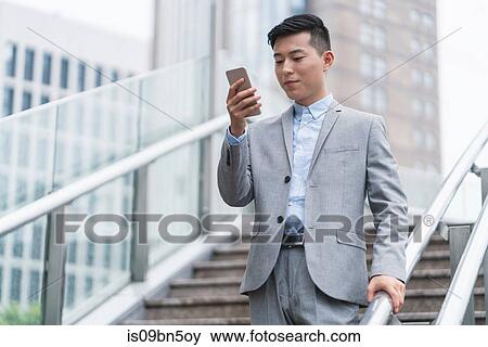 Young businessman looking at smartphone on city stairway, Shanghai, China View Large Photo Image Stock Photo - Young businessman looking at smartphone on city stairway, Shanghai, China. Fotosearch
