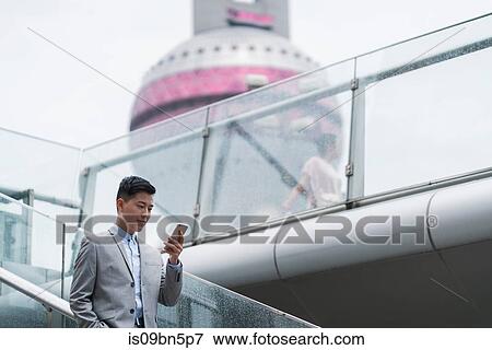 Young businessman looking at smartphone on city stairway, Shanghai, China View Large Photo Image Stock Photo - Young businessman looking at smartphone on city stairway, Shanghai, China. Fotosearch
