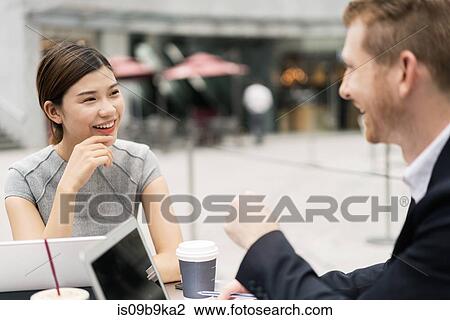 Stock Image - Young businesswoman and man having discussion at sidewalk cafe. Fotosearch