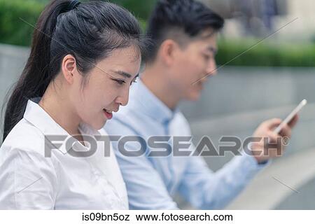 Stock Photo - Young businesswoman and man looking at smartphone in city, Shanghai, China. Fotosearch