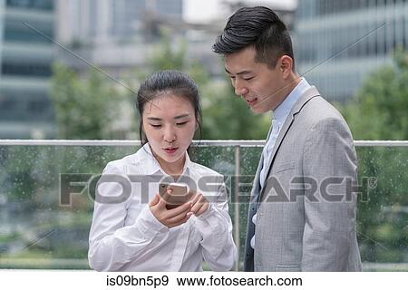 Young businesswoman and man looking at smartphone in city, Shanghai, China View Large Photo Image Stock Photo - Young businesswoman and man looking at smartphone in city, Shanghai, China. Fotosearch