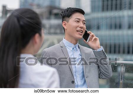 Young businesswoman and man talking on smartphone in city, Shanghai, China View Large Photo Image Stock Photo - Young businesswoman and man talking on smartphone in city, Shanghai, China. Fotosearch