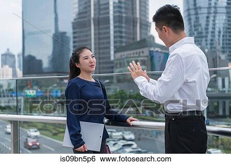 Stock Photograph - Young businesswoman and man talking on balcony in city financial district, Shanghai, China. Fotosearch