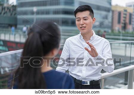 Stock Photography - Young businesswoman and man talking on balcony in city financial district, Shanghai, China. Fotosearch