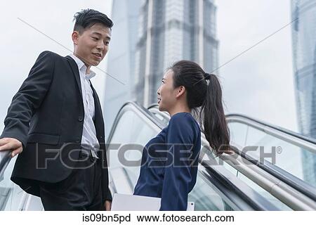 Young businesswoman and man talking while moving up city escalator, Shanghai, China View Large Photo Image Stock Image - Young businesswoman and man talking while moving up city escalator, Shanghai, China. Fotosearch