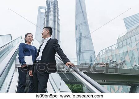 Young businesswoman and man talking while moving up city escalator, Shanghai, China View Large Photo Image Stock Image - Young businesswoman and man talking while moving up city escalator, Shanghai, China. Fotosearch