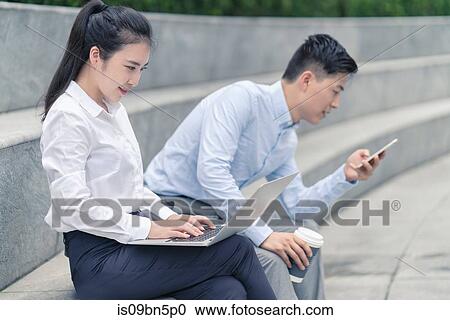 Young businesswoman and man using laptop and looking at smartphone on city seat, Shanghai, China View Large Photo Image Stock Image - Young businesswoman and man using laptop and looking at smartphone on city seat, Shanghai, China. Fotosearch