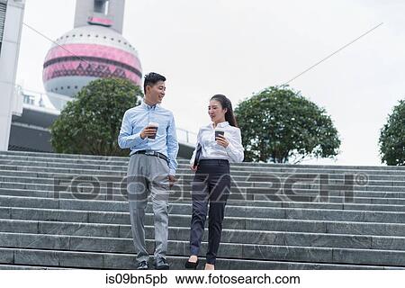 Stock Image - Young businesswoman and man with takeaway coffee moving down city stairway, Shanghai, China. Fotosearch