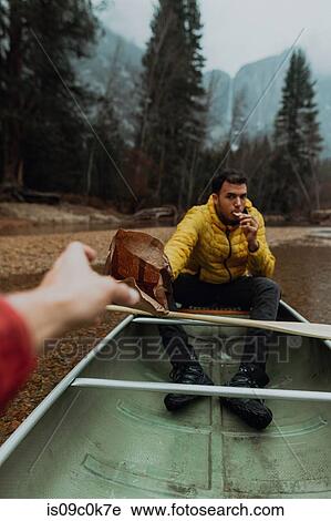 Stock Image - Young canoeing couple sharing snacks on canoe, personal perspective, Yosemite Village, California, USA. Fotosearch