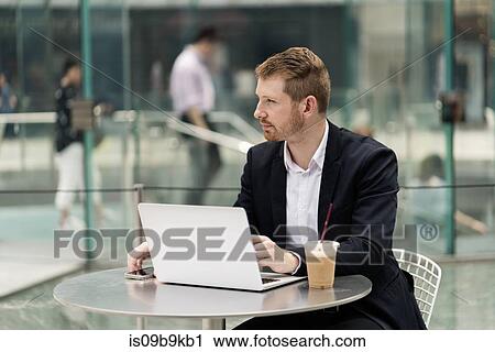 Stock Image - Young city businessman at sidewalk cafe looking away. Fotosearch