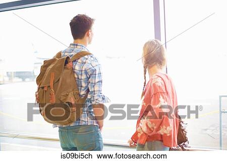 Young couple at airport, carrying backpacks, looking out of window View Large Photo Image Stock Image - Young couple at airport, carrying backpacks, looking out of window. Fotosearch