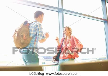 Stock Image - Young couple at airport, man photographing woman using smartphone. Fotosearch