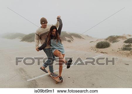 Young couple holding hands sharing a skateboard in beach carpark, Jalama, California, USA View Large Photo Image Stock Image - Young couple holding hands sharing a skateboard in beach carpark, Jalama, California, USA. Fotosearch