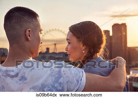 Stock Photo - Young couple in front of skyline at sunset roof party in London, UK. Fotosearch