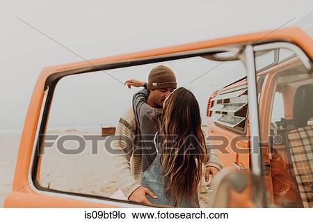 Picture - Young couple kissing by recreational vehicle at beach, Jalama, California, USA. Fotosearch