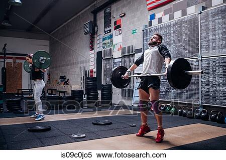 Stock Photography - Young couple lifting barbell in gym. Fotosearch
