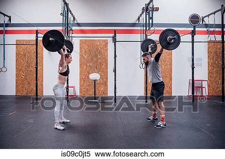 Stock Photography - Young couple lifting barbell in gym. Fotosearch