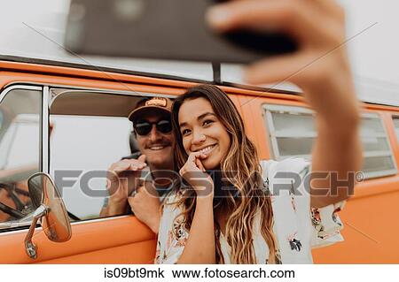 Stock Image - Young couple on road trip in recreational vehicle taking smartphone selfie, portrait, Jalama, California, USA. Fotosearch