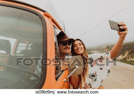 Stock Image - Young couple on roadside in recreational vehicle taking smartphone selfie, portrait, Jalama, California, USA. Fotosearch