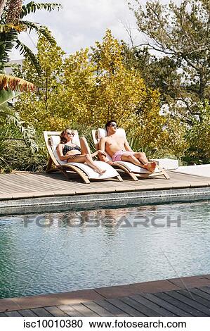 Stock Image - Young couple relaxing on deckchair by swimming pool. Fotosearch