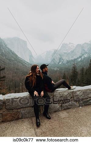 Young couple sitting on wall in mountain landscape, Yosemite Village, California, USA View Large Photo Image Stock Photo - Young couple sitting on wall in mountain landscape, Yosemite Village, California, USA. Fotosearch