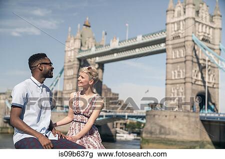 Young couple sitting on wall, smiling, Tower Bridge in background, London, England, UK View Large Photo Image Stock Image - Young couple sitting on wall, smiling, Tower Bridge in background, London, England, UK. Fotosearch