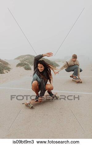 Stock Image - Young couple skateboarding in misty beach carpark, Jalama, California, USA. Fotosearch