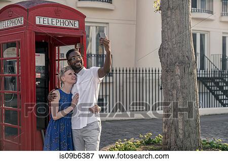 Young couple standing beside red telephone box, looking up, smiling View Large Photo Image Stock Photo - Young couple standing beside red telephone box, looking up, smiling. Fotosearch
