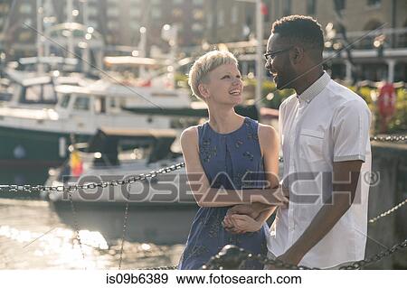 Stock Photo - Young couple walking beside dock, hand in hand, smiling. Fotosearch