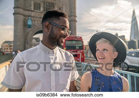 Picture - Young couple walking outdoors, Tower Bridge in background. Fotosearch