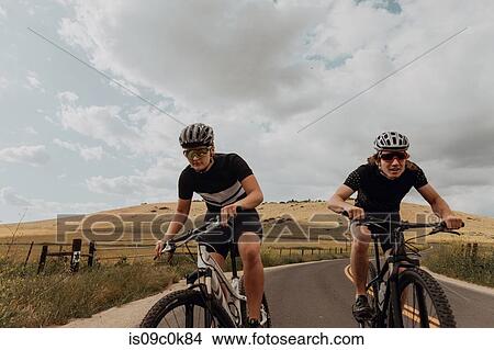 Picture - Young cycling couple cycling on rural road, Exeter, California, USA. Fotosearch