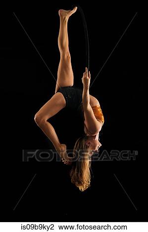 Young female aerial acrobat hanging upside down from hoop against black background View Large Photo Image Stock Image - Young female aerial acrobat hanging upside down from hoop against black background. Fotosearch