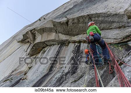 Stock Image - Young female rock climber climbing rock face, low angle view, The Chief, Squamish, British Columbia, Canada. Fotosearch