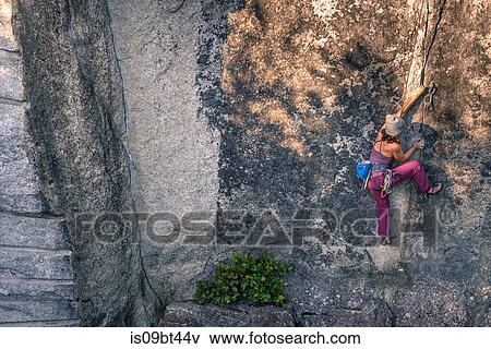Stock Photo - Young female rock climber climbing rock face, high angle view, Smoke Bluffs, Squamish, British Columbia, Canada. Fotosearch
