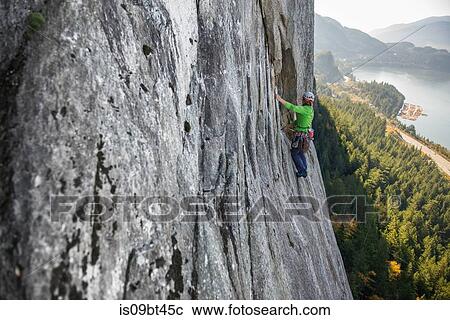 Stock Image - Young female rock climber climbing up rock face, elevated view, The Chief, Squamish, British Columbia, Canada. Fotosearch