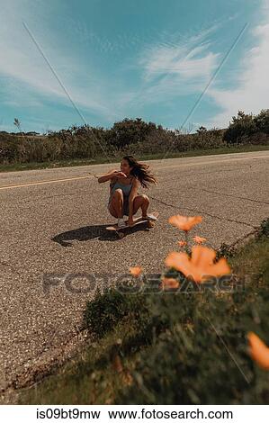 Young female skateboarder crouch skateboarding along rural road, Jalama, California, USA View Large Photo Image Stock Photo - Young female skateboarder crouch skateboarding along rural road, Jalama, California, USA. Fotosearch