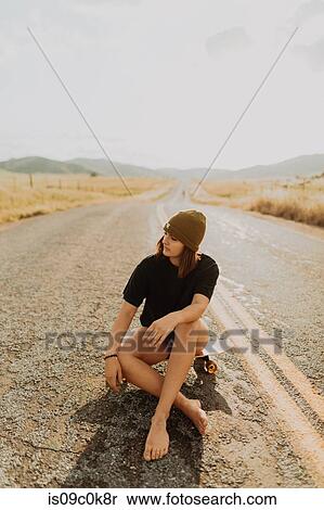 Stock Photography - Young female skateboarder sitting on rural road, Exeter, California, USA. Fotosearch