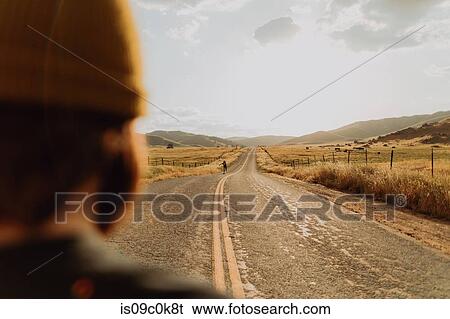 Stock Photograph - Young female skateboarder skateboarding on rural road, over shoulder view, Exeter, California, USA. Fotosearch