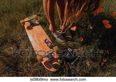 Picture - Young female skateboarder tying shoelaces in grass, Jalama, California, USA. Fotosearch