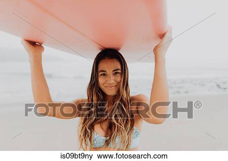 Young female surfer carrying surfboard on head at beach, portrait, Ventura, California, USA View Large Photo Image Stock Photo - Young female surfer carrying surfboard on head at beach, portrait, Ventura, California, USA. Fotosearch