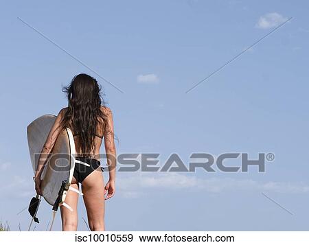 Young female surfer carrying surfboard looking out at blue sky from beach, rear view, Victoria, Australia View Large Photo Image Stock Photo - Young female surfer carrying surfboard looking out at blue sky from beach, rear view, Victoria, Australia. Fotosearch