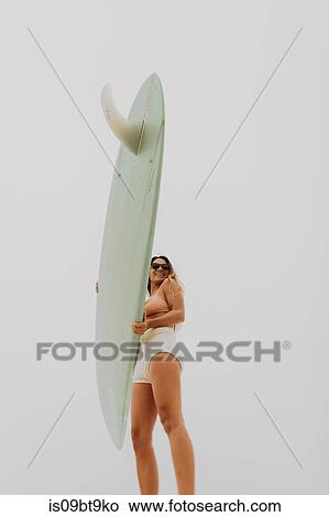 Picture - Young female surfer holding surfboard, low angle view, Jalama, Ventura, California, USA. Fotosearch