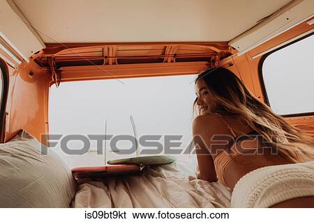 Stock Photograph - Young female surfer in bikini lying in back of recreational vehicle at beach, Jalama, California, USA. Fotosearch