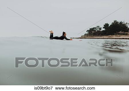 Young female surfer lying on surfboard in misty calm sea, Ventura, California, USA View Large Photo Image Stock Photo - Young female surfer lying on surfboard in misty calm sea, Ventura, California, USA. Fotosearch