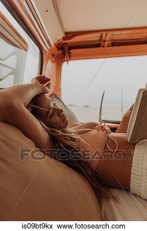 Stock Photo - Young female surfer reading book in back of recreational vehicle at beach, Jalama, California, USA. Fotosearch