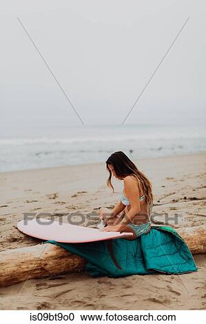 Young female surfer sitting on log waxing surfboard at beach, Ventura, California, USA View Large Photo Image Stock Image - Young female surfer sitting on log waxing surfboard at beach, Ventura, California, USA. Fotosearch